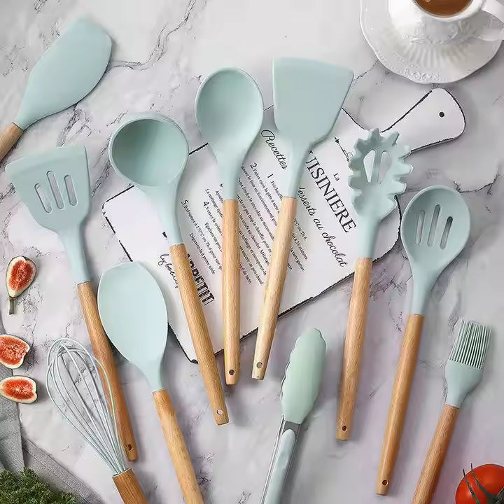 Set of kitchen utensils with light blue silicone heads and wooden handles on a marble surface.