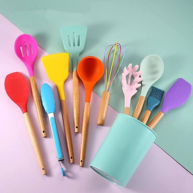 Colorful kitchen utensils with wooden handles in a teal holder on a pastel background