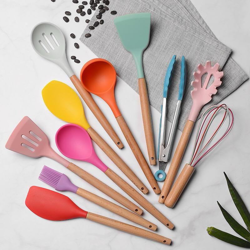 Colorful kitchen utensils including spatulas, spoons, and tongs on a light gray background.