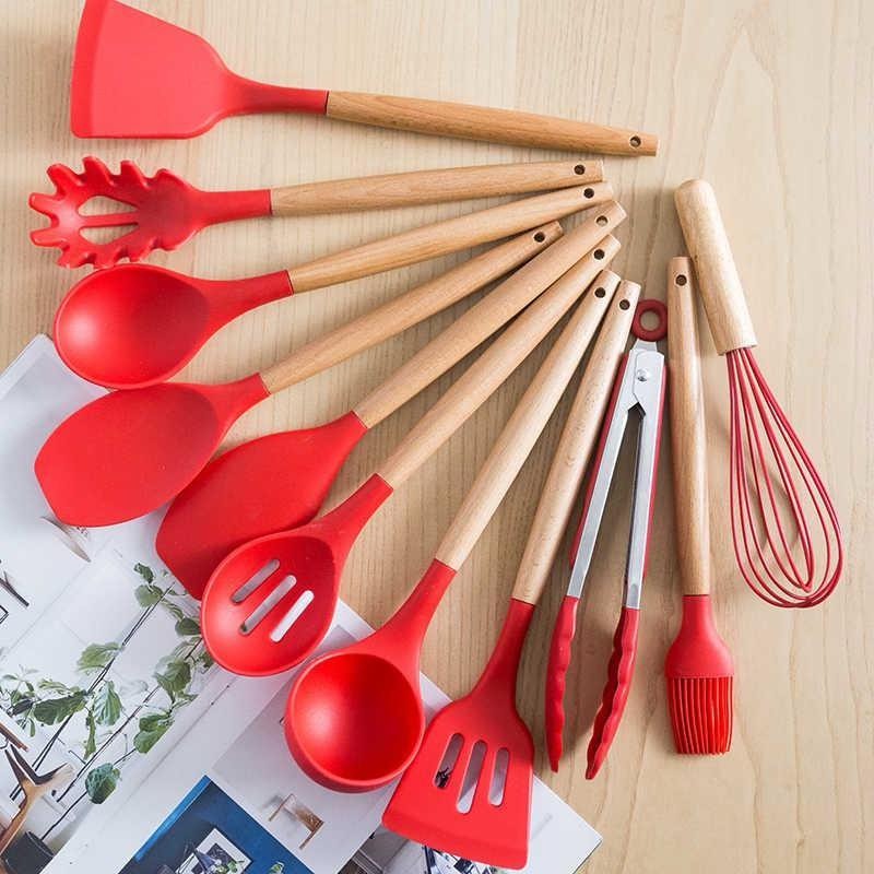 Set of red kitchen utensils with wooden handles on a light wood surface.