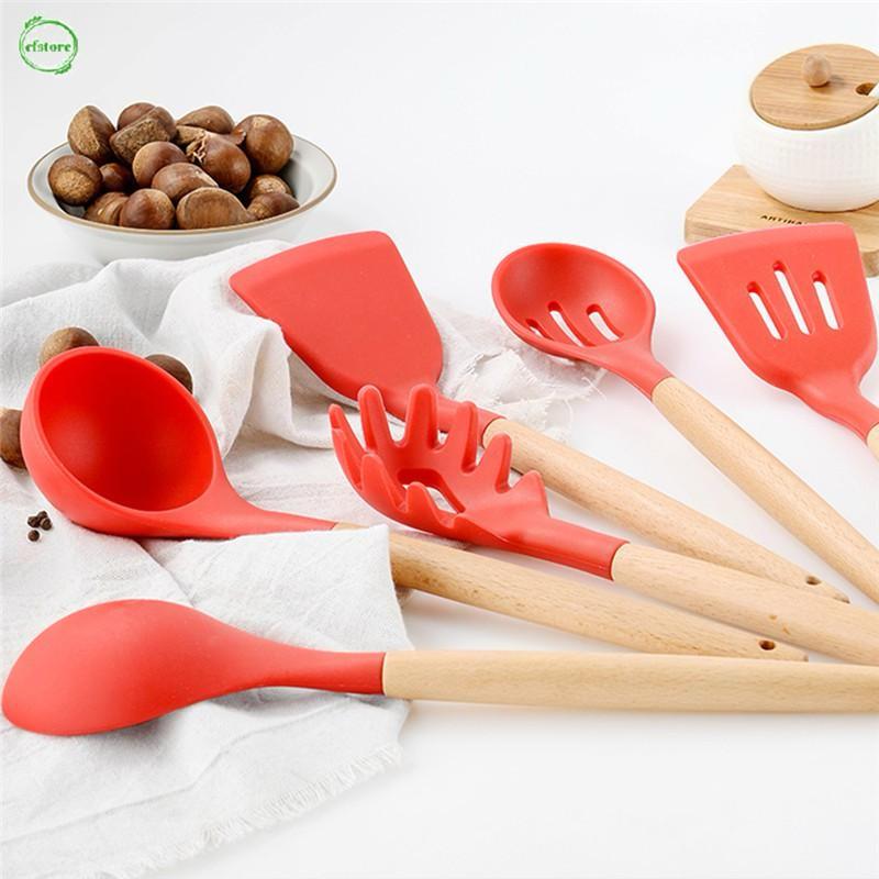 Set of red silicone kitchen utensils with wooden handles on a white surface.