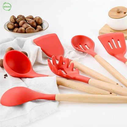 Set of red silicone kitchen utensils with wooden handles on a white surface.